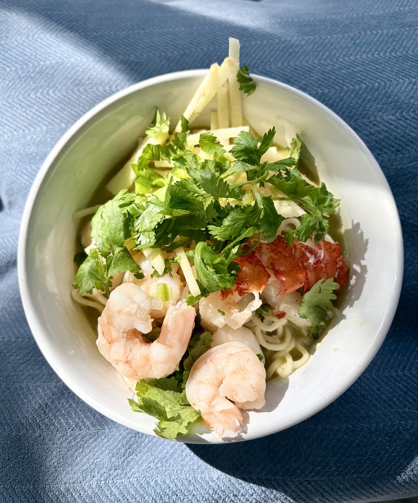 Bowl of homemade coconut green curry ramen topped with shrimp, cilantro, and vegetables.