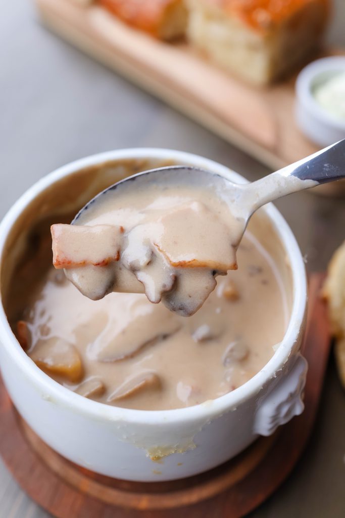 Bowl of creamy mushroom soup with a spoonful of soup and mushrooms lifted above the bowl.