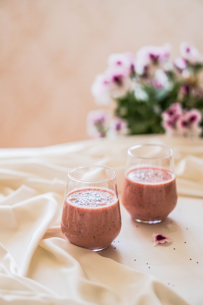 Two mixed berry smoothies on a table with flowers in the background.