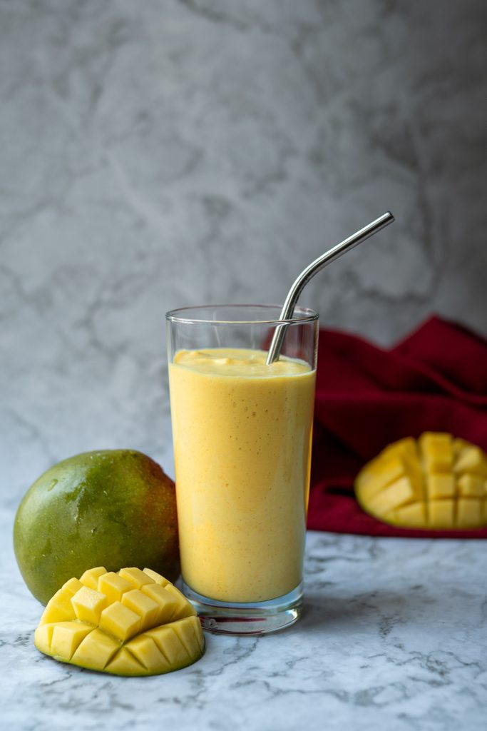 Mango pineapple smoothie with fruits in the background.