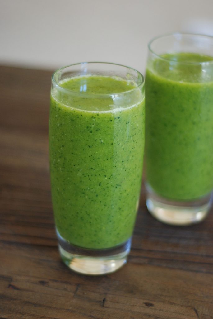 Two strawberry kale smoothies in glasses on a table.