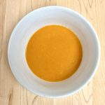 Buffalo Sauce in a white bowl on a cutting board.