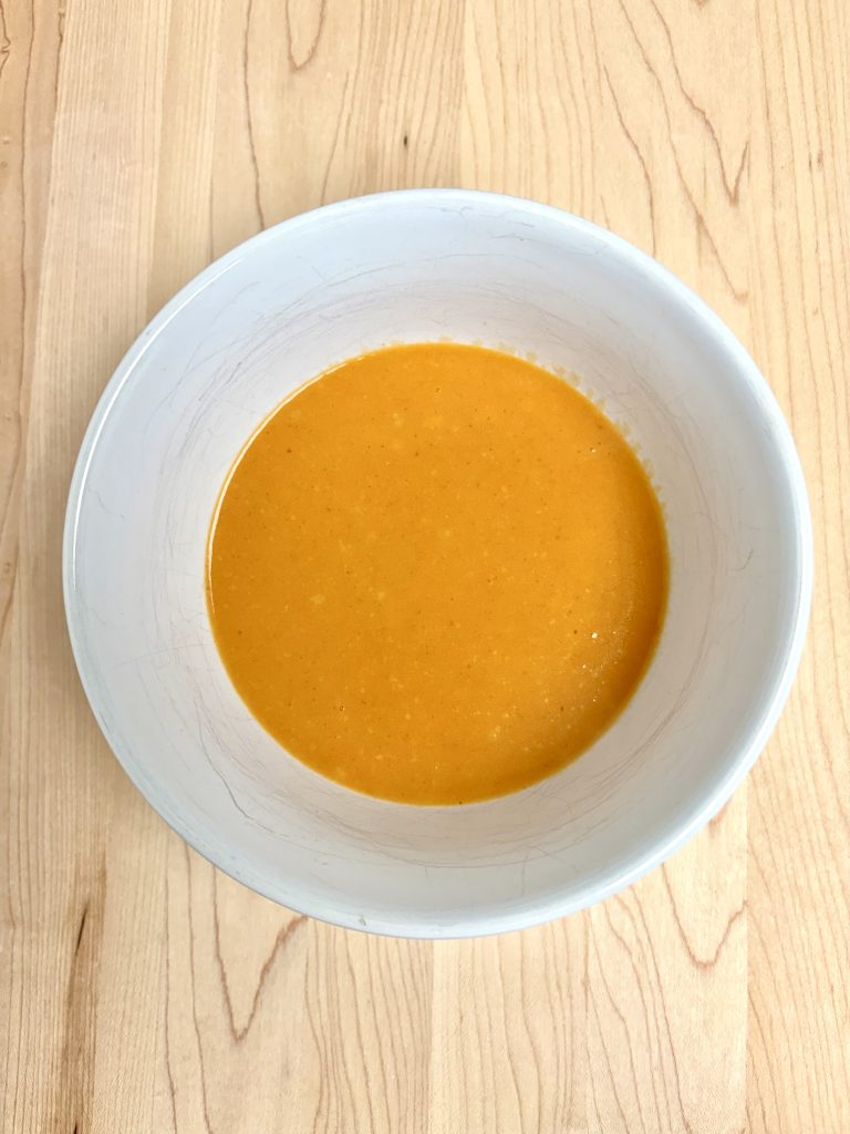 Buffalo Sauce in a white bowl on a cutting board.