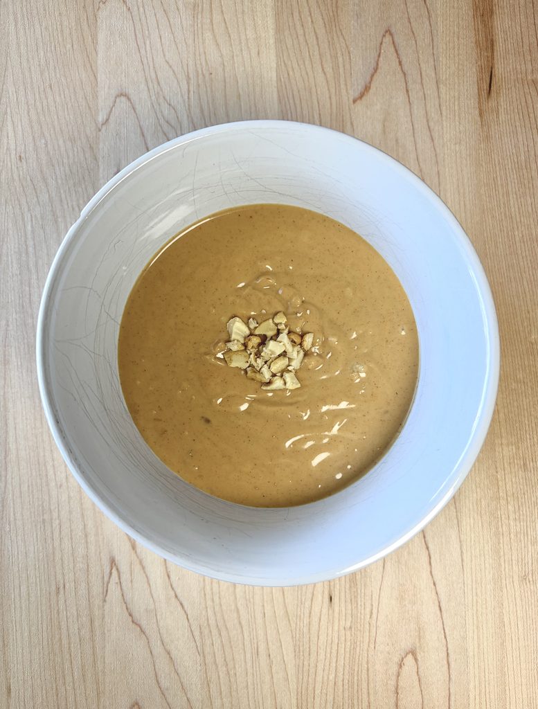 Peanut sauce in a white bowl with peanuts.